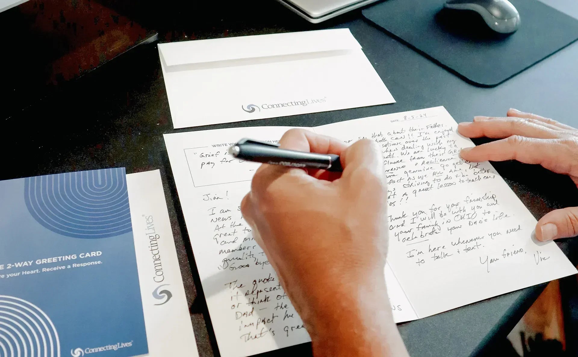Person writing a heartfelt letter with a ConnectingLives 2-Way Greeting Card and envelope on a desk